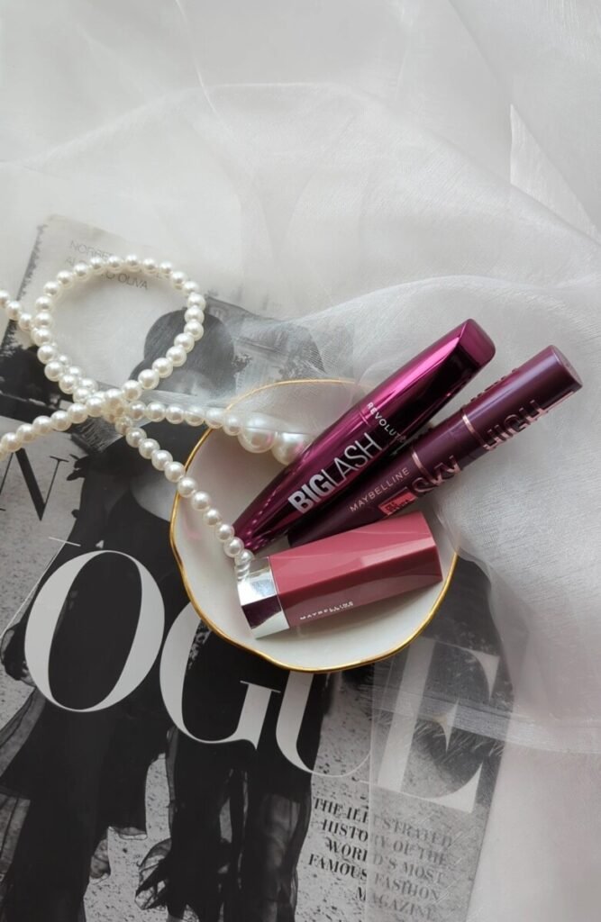 Burgundy mascara and nude lipstick arranged over a black-and-white fashion portrait with sheer fabric, blending modern beauty and timeless elegance.